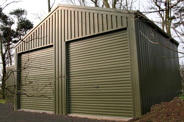 A green building with two roller doors nestled in amongst trees in winter